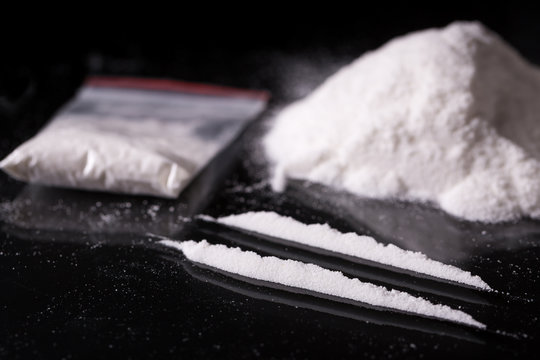 Plastic packet, two lines and pile of cocaine on black background