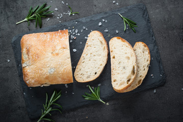 Italian ciabatta bread  on black slate with herbs and olives. - obrazy, fototapety, plakaty