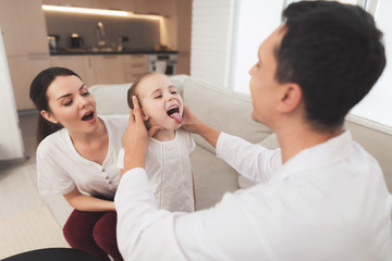 The little girl caught a cold. Her mother called the doctor at home. Doctor looks at the girl's throat