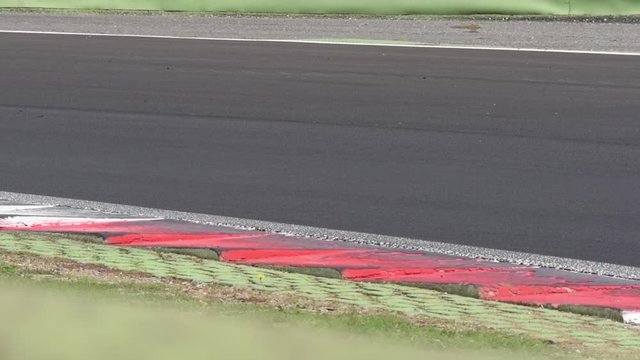 Motorsport circuit track round and curb closeup with blurred car racing crossing left to right