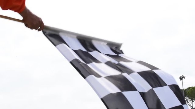 Slow motion waving checkered flag, closeup of motorsport symbol of win, finish line, end of the race, low angle view sky in background