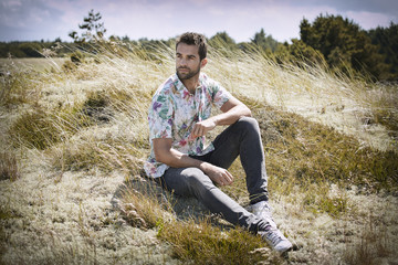 Naklejka na ściany i meble Handsome guy in floral shirt sitting in meadow