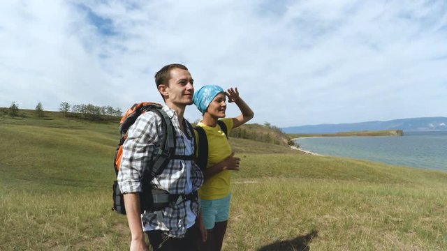 Hikers man and woman trekking walking with backpacks along Lake Baikal pointing at blue lake