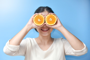 Woman holding sliced orange on her eyes.
