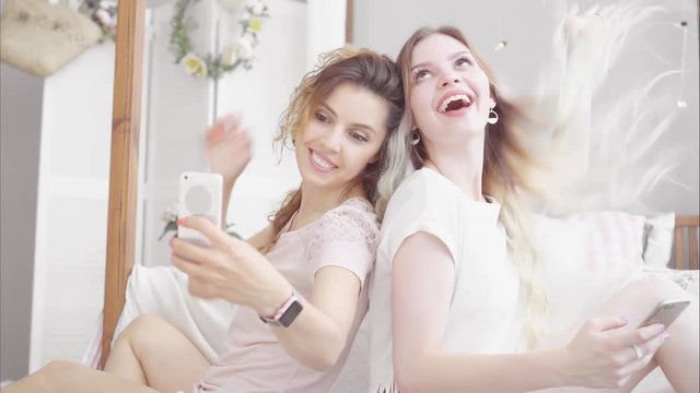 Young women friends make selfie with smartphone in the bedroom near the bed
