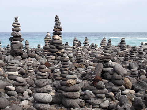 pebbles and stones arranged into many tall stacked shapes in shades of grey on a beach