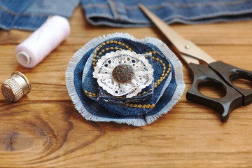 Denim flower jewellery. Scissors, thread, thimble, needle, female old jeans on a wooden background. What to do with old jeans. Recycled crafts for kids. Closeup