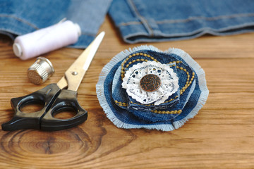 Fototapeta na wymiar Handmade denim flower jewellery. Scissors, thread, thimble, needle, female old jeans on a wood background. Sewing projects to recycle old jeans. Closeup