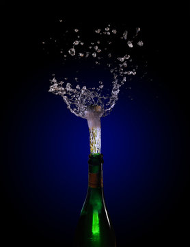 champagne bottle explosion with cork popping splash against a dark background with blue to black gradient, copy space