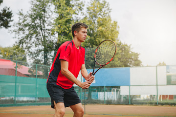 Handsome man in shirt holding tennis racket and looking concentrated while standing on tennis court