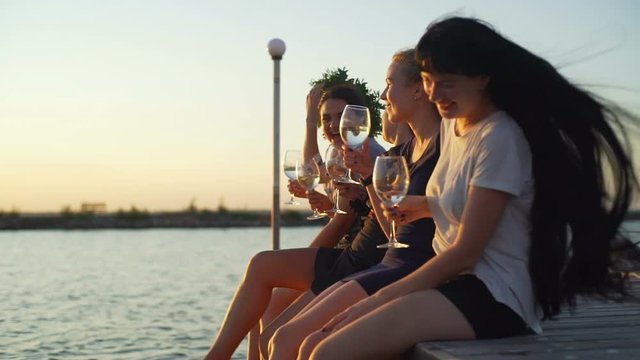 Girls sitting at pier laughing drink wine seaside sunrise rapid slow motion