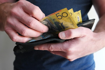 A man pulling out cash from wallet and counting fifty Australian dollar bills cash on hand to ready...
