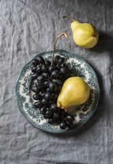Fresh ripe grapes and pears on a vintage plate on a gray background, top view