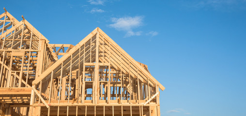 Close-up of gables roof on stick built home under construction and blue sky in Humble, Texas, USA. New build roof with wooden truss, post and beam framework. Timber frame house, real estate. Panorama - Powered by Adobe