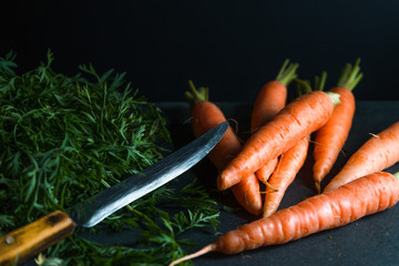 Orange carrots, leaves and a knife on a dark blue background