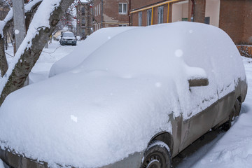 Parked snow-covered cars near houses in the courtyard in winter morning.