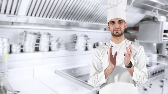 Young Caucasian chef wearing uniform and applauding in the kitchen