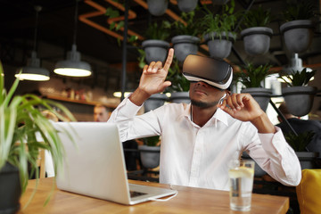 African man playing game in head seat, pointing by fingers in air.