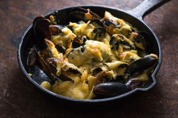 Cooked mussels in a cast-iron frying pan with cheese sauce