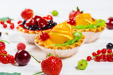 Delicious fruit cake on white wooden background with strawberries, cherries, currants and raspberries. Beautiful, delightful and healthy desserts