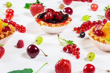 Delicious fruit cake on white wooden background with strawberries, cherries, currants and raspberries. Beautiful, delightful and healthy desserts