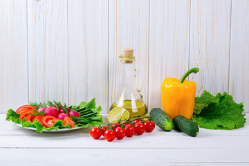 Cucumbers, radish, tomatoes cherry, olive oil, herb and spices on old white wooden background. Set for healthy foods. Ingredients for salad.