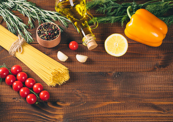 Spaghetti, tomatoes cherry, olive oil, herb and spices on old brown wooden background.