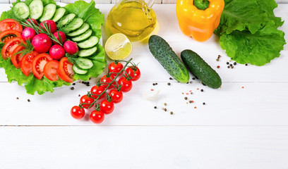 Cucumbers, radish, tomatoes cherry, olive oil, herb and spices on old white wooden background. Set for healthy foods. Ingredients for salad.