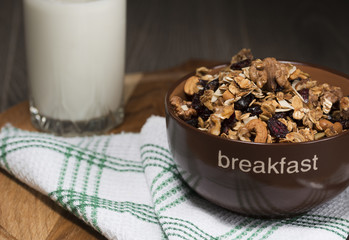 Homemade granola with honey, oatmeal, cashew nut, almond, pistachio, raisin and cranberry in clay bowl,glass with milk on wood dark table,