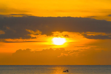 The sun shines through the clouds at dawn on the shore of the Gulf of Thailand.