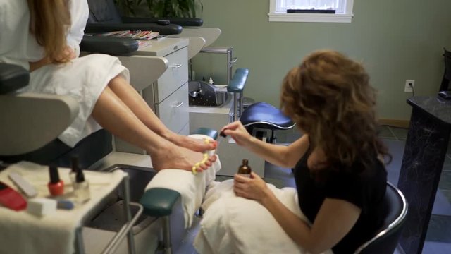 With toe spacers in place, pedicurist paints toenails with red polish.  Steadicam shot.