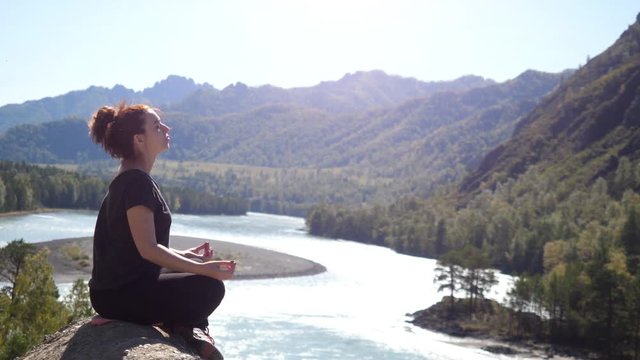 Young woman with red hair meditating in the beautiful mountains and mountain river view. 4k, 3840x2160