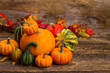 pile of raw orange and green pumpkins harvest with fall leaves on wooden table