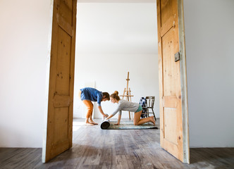 Young couple moving in new house, rolling out carpet.