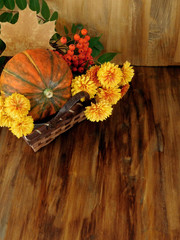Pumpkin in a wicker basket with flowers, rowan and dry leaves. Autumn still life