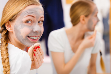 Woman removing mud facial mask with sponge