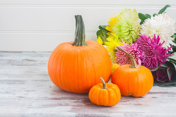 ripe of orange pumpkins with fall flowers on white wooden table with copy space