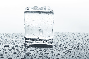 Transparent ice cube on glass with water drops