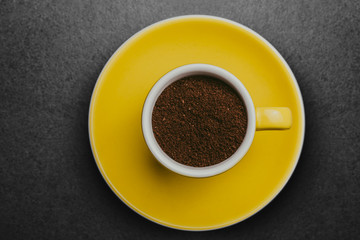 Espresso cup filled with coffee powder on yellow plate background.