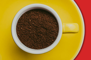 Espresso cup filled with coffee powder on yellow plate isolated on red background.
