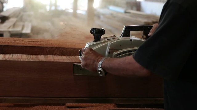 Senior worker using electric planer with wooden plank in carpentry workshop