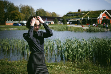 street portrait of a student girl dressed fashionably in dark clothes, against a pond background in the autumn sunny day