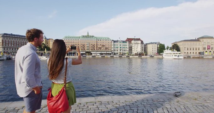 Tourist taking photo using smart phone in Stockholm cityscape and Gamla Stan. Woman photographer taking photos using smartphone. Couple traveling sightseeing visiting landmarks in Sweden, Scandinavia.