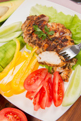 Chicken fillet with avocado and some vegetable on the side (tomato, cucumber, bell pepper) on a white background eaten with a fork