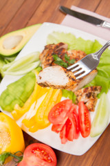 Chicken fillet with avocado and some vegetable on the side (tomato, cucumber, bell pepper) on a white background eaten with a fork