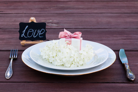 Aster flower on a plate with a box of jewelry present, next to a silver fork and knife.	