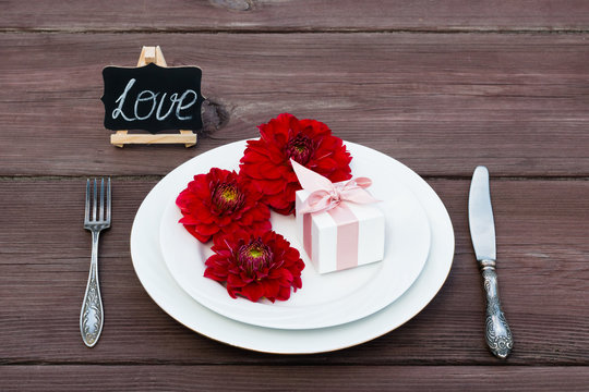 Aster flower on a plate with a box of jewelry present, next to a silver fork and knife.	