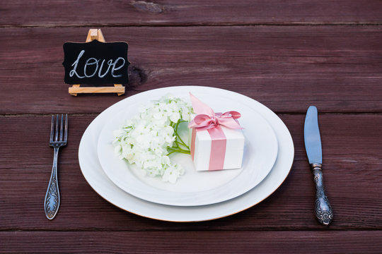 Aster flower on a plate with a box of jewelry present, next to a silver fork and knife.	