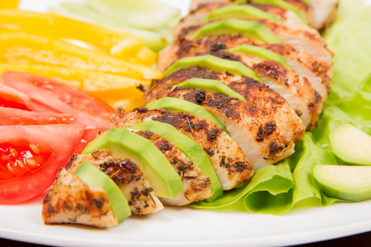 Chicken fillet with avocado and some vegetable on the side (tomato, cucumber, bell pepper) on a wooden background