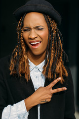 Victory gesture. Joyful young black lady. Happy African American woman, stylish model posing on dark background, happiness concept